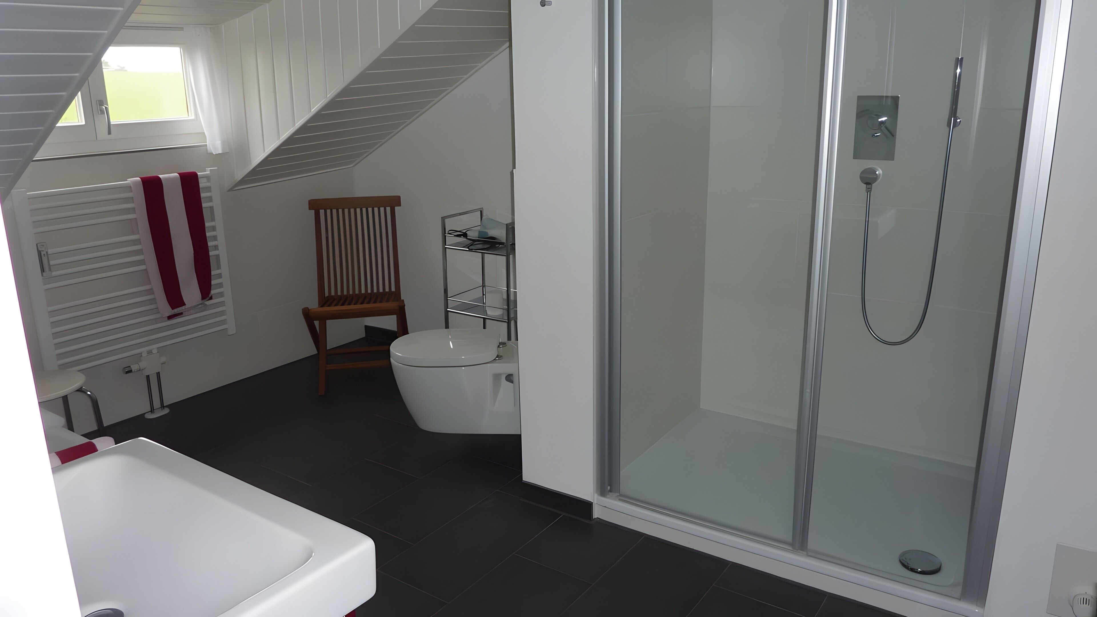 A modern bathroom with a glass-enclosed shower, a white toilet, and a wooden chair.
