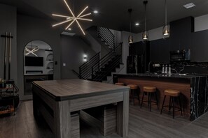 A modern kitchen with a wooden table, bar stools, and a staircase. - META Royal Estate~>THE KAWS HAUS! By Yasmeen (Houston)