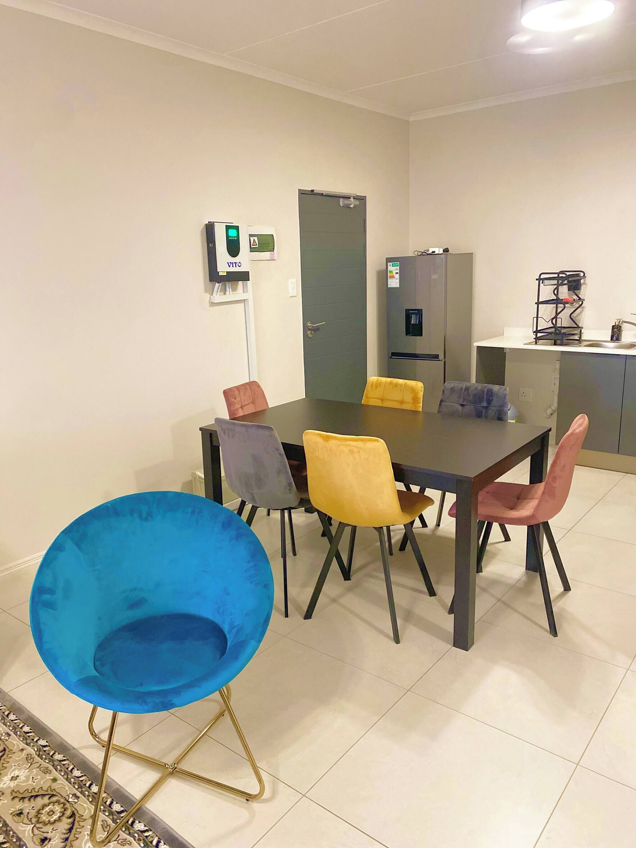 Zona pranzo con tavolo, sedie, frigorifero, dispenser di acqua e un dispositivo VITO a parete.