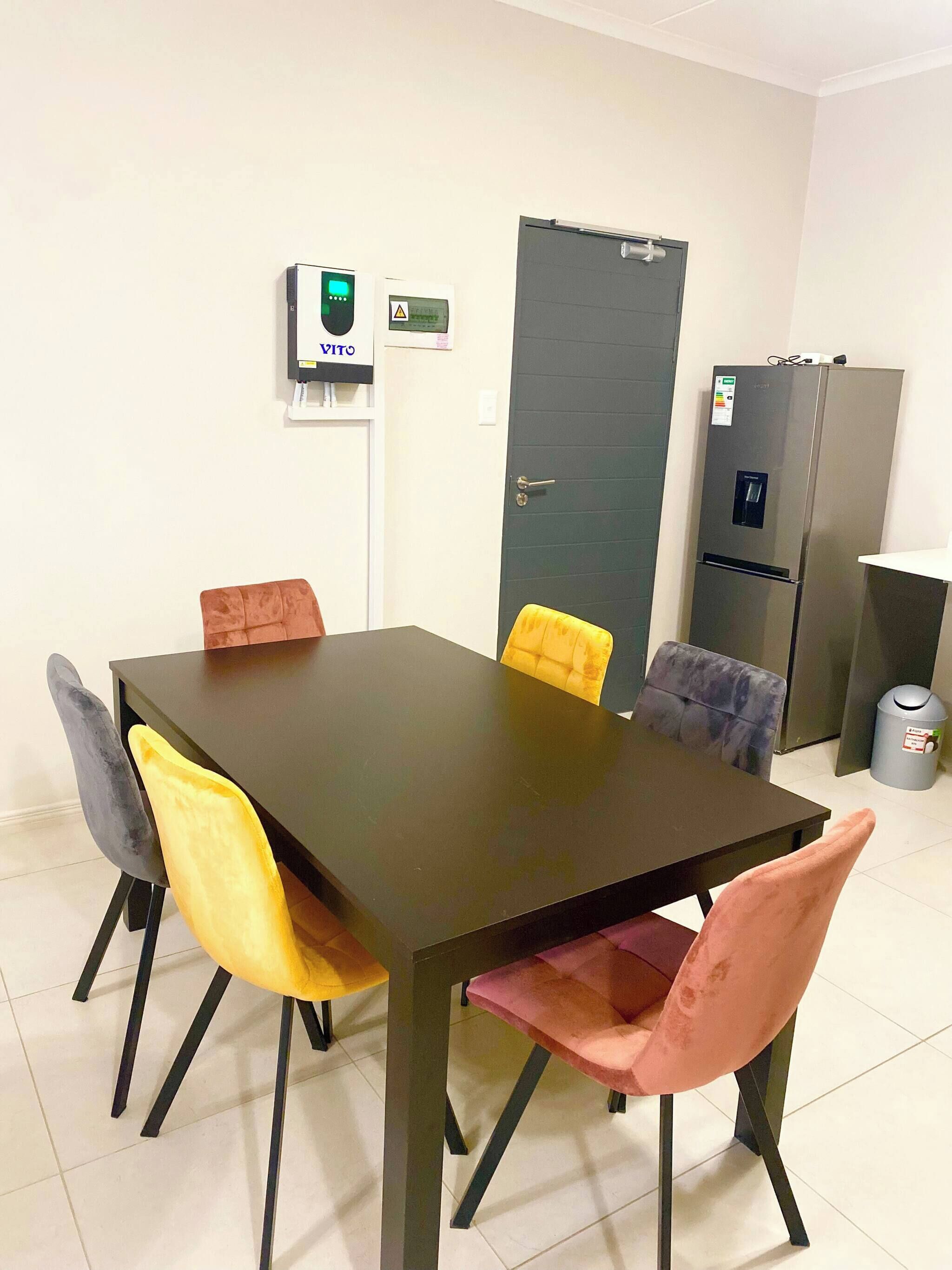 A conference room with a dark table, four chairs, a door, and a refrigerator.