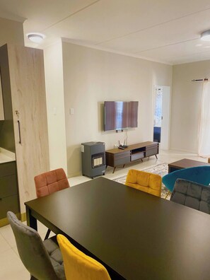 A modern living room with a dining table, sofas, a TV, and a built-in heater. - Blest5 Tranquil Stay 1 (Johannesburg)