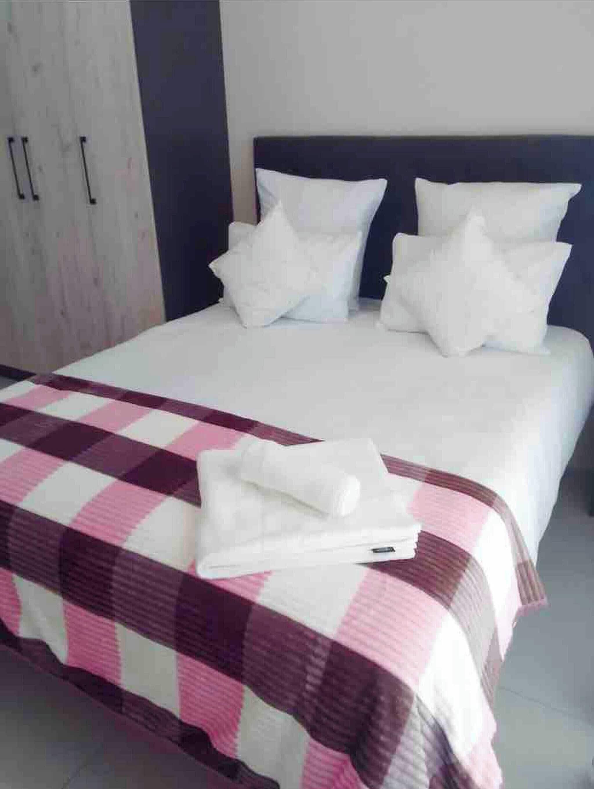 A bed with white bedding and a checkered blanket, a dark headboard, and a wardrobe with handles.