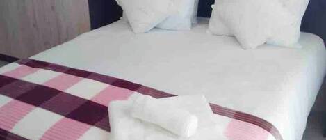 A bed with white bedding and a checkered blanket, a dark headboard, and a wardrobe with handles.