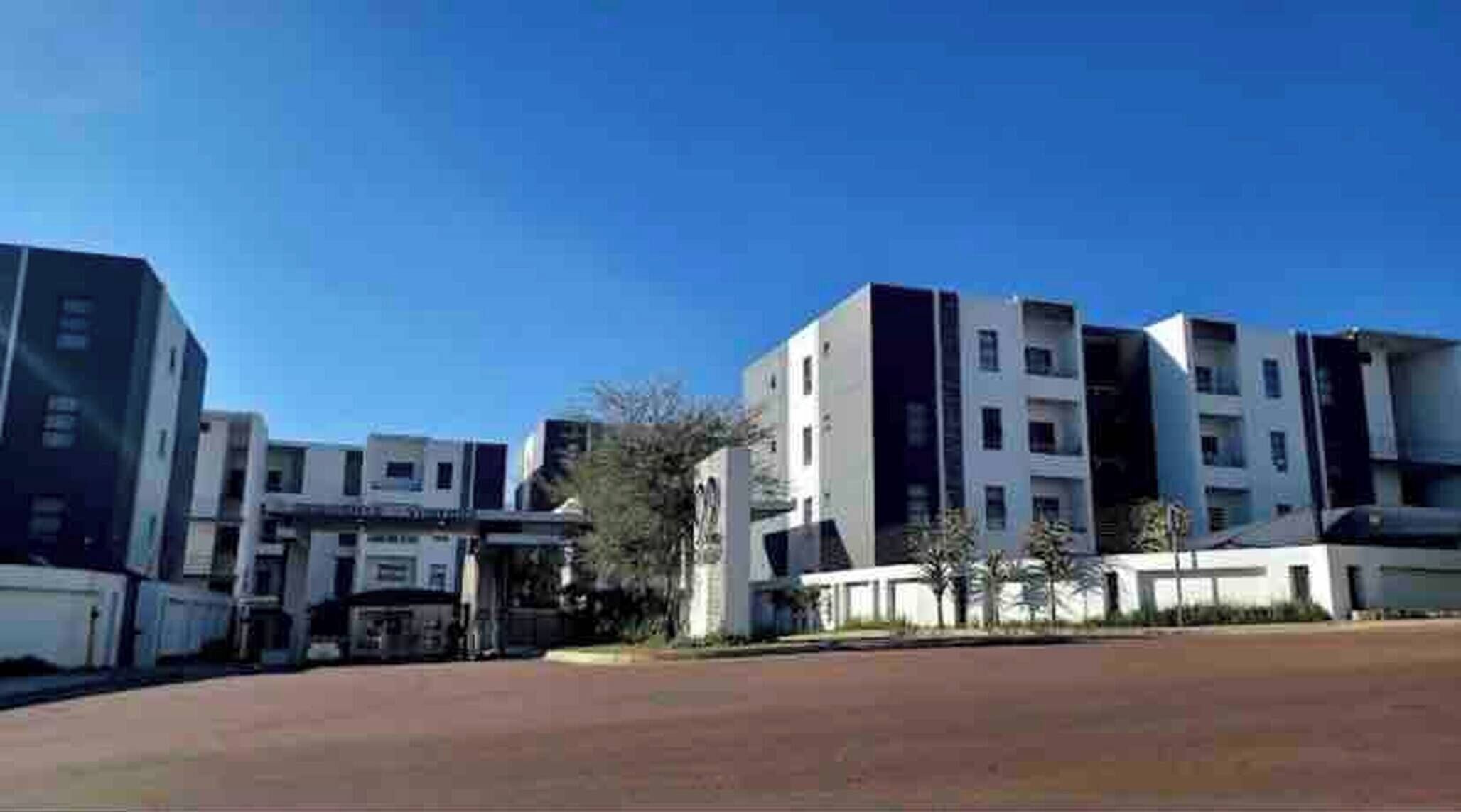 A modern building complex with multiple floors, a central entrance, and a paved area in front.