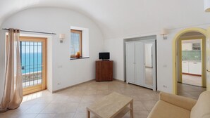 Amplia sala de estar con vista al mar, un armario de madera, un televisor y una puerta que da a la cocina.