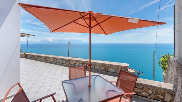 Una terraza con mesa y sillas, un paraguas grande y vista al mar.