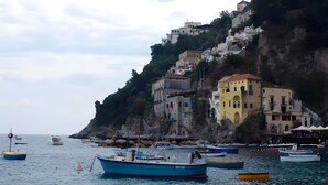 Un pueblo costero con edificios sobre un acantilado, barcos en el agua y una costa rocosa.
