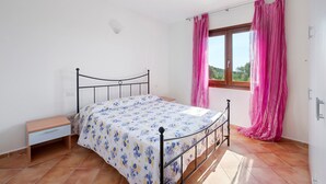 Una camera da letto con un letto, un comodino, una finestra con tende e vista sul verde.