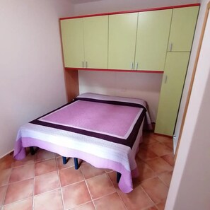 A small room with a bed, a green wardrobe, and a tiled floor. - Apartment 'Lu Sulianu- T2' with Private Terrace, Private Garden and Air Conditioning (Budoni)