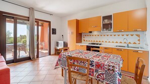 Una cucina compatta con mobili arancioni, un tavolo da pranzo con una tovaglia colorata e una porta vetrata scorrevole che dà su uno spazio esterno.