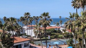 Uma piscina com espreguiçadeiras, quadra de tênis e vista para o mar.