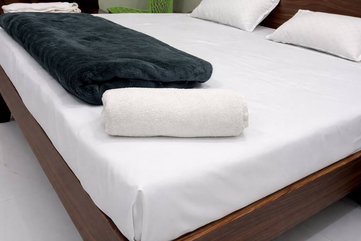 A neatly made bed with white sheets, a dark grey blanket, and a white towel.