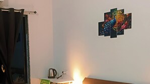 A hotel room with a bed, a nightstand, a lamp, a painting, and a window with curtains. - Varad International Hotel and Banquet (Alapur)
