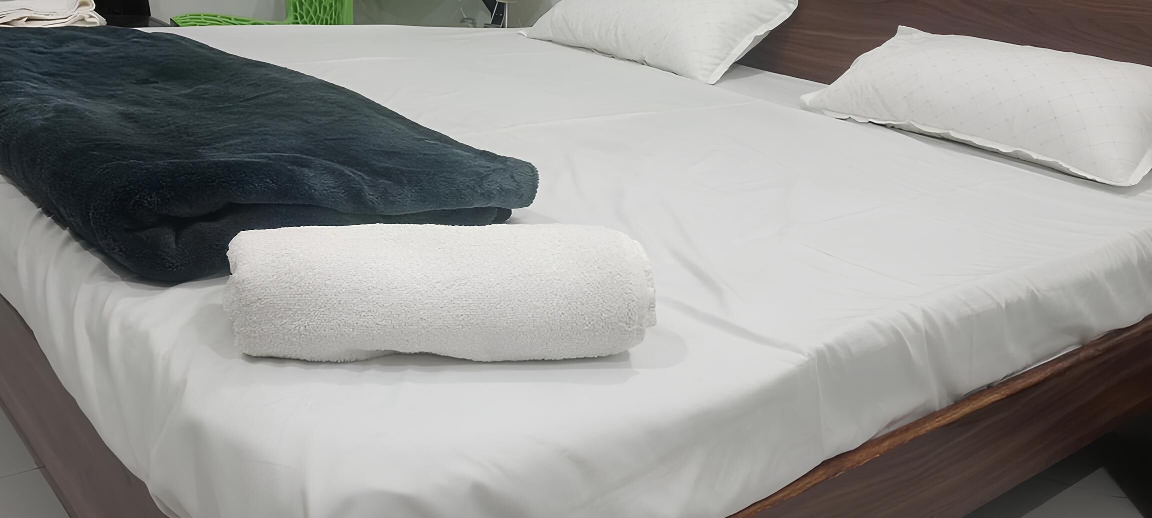 Un llit ben fet amb llençols blancs, una manta blau fosc i una tovallola blanca.