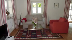 Una sala de estar con un sofá, un sillón rojo, una mesa de centro con un jarrón, una lámpara y un radiador.