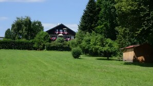 Ein großes Haus mit einem gepflegten Rasen und einem Holzgebäude zur rechten Seite.