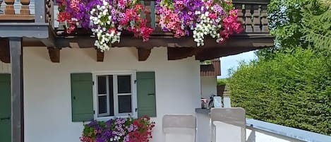 Un balcón con macetas colgantes de flores y una ventana con persianas.