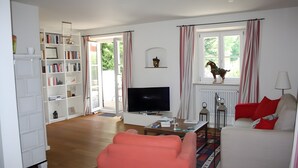 Ein Wohnzimmer mit Fernseher, einer Couch, einem Bücherregal und einem Fenster mit Vorhängen.