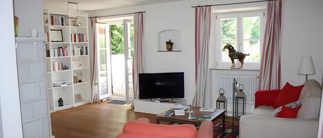Una sala de estar con televisor, sofá, estantería y una ventana con cortinas.
