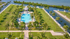 Luchtbeeld van een resort met een centraal zwembad, omgeven door palmbomen en een waterpartij.