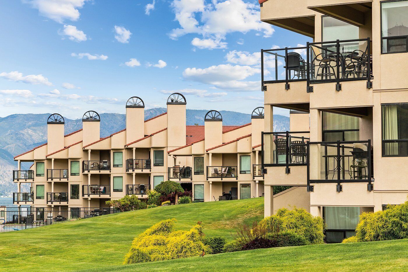 A multi-story hotel with balconies, a pool, and a mountainous backdrop.