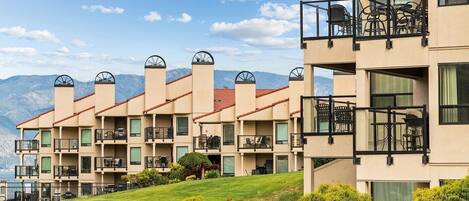 A multi-story hotel with balconies, a pool, and a mountainous backdrop.