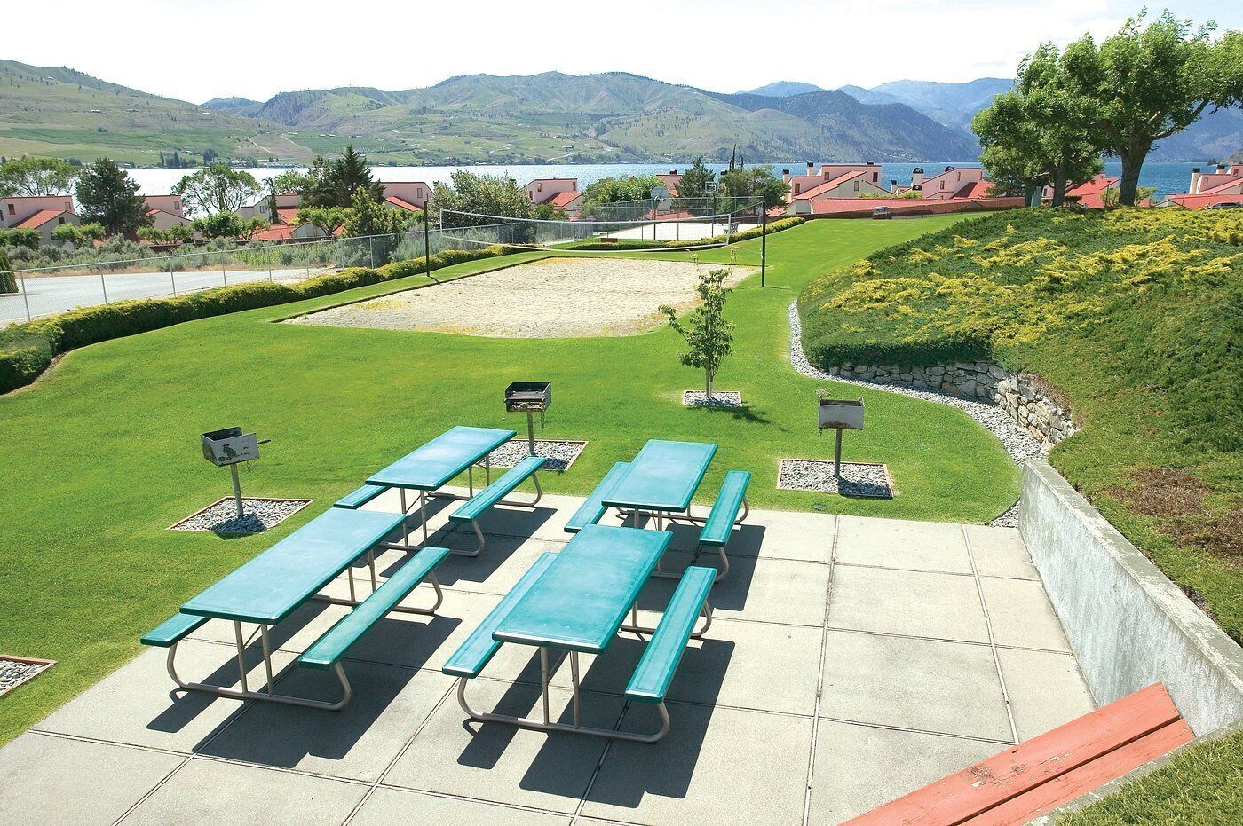 Un espace pique-nique aménagé avec des tables et des bancs, entouré d’un jardin paysager offrant une vue sur les montagnes et un lac.