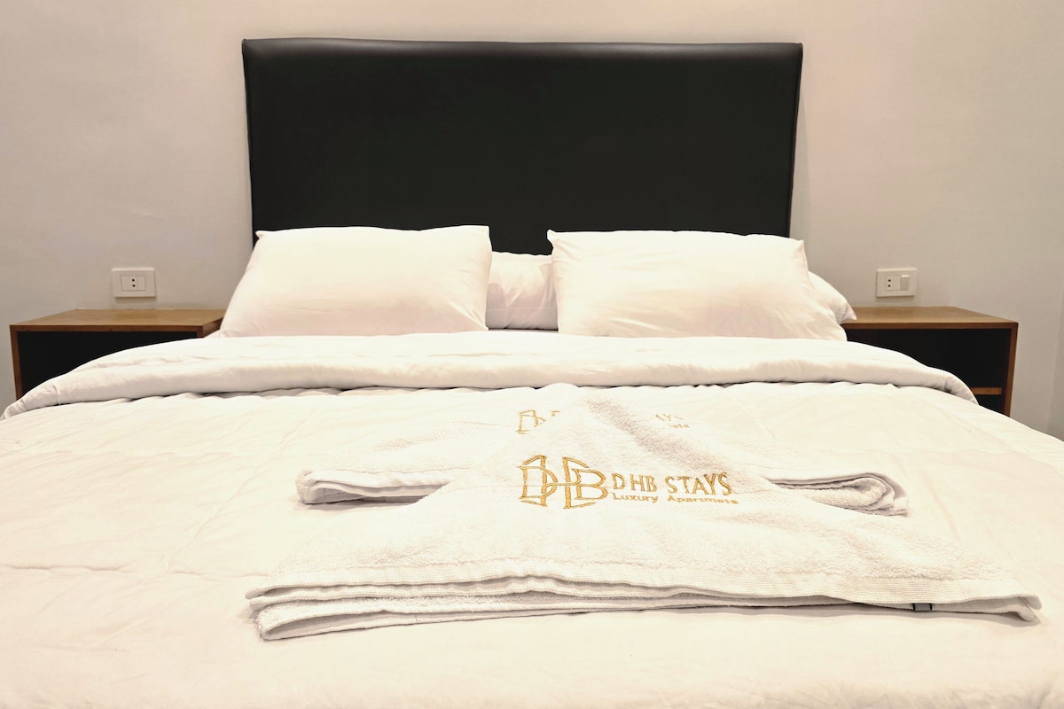 Een opgemaakt bed met een zwart hoofdeinde, wit beddengoed en een handdoek met tekst.