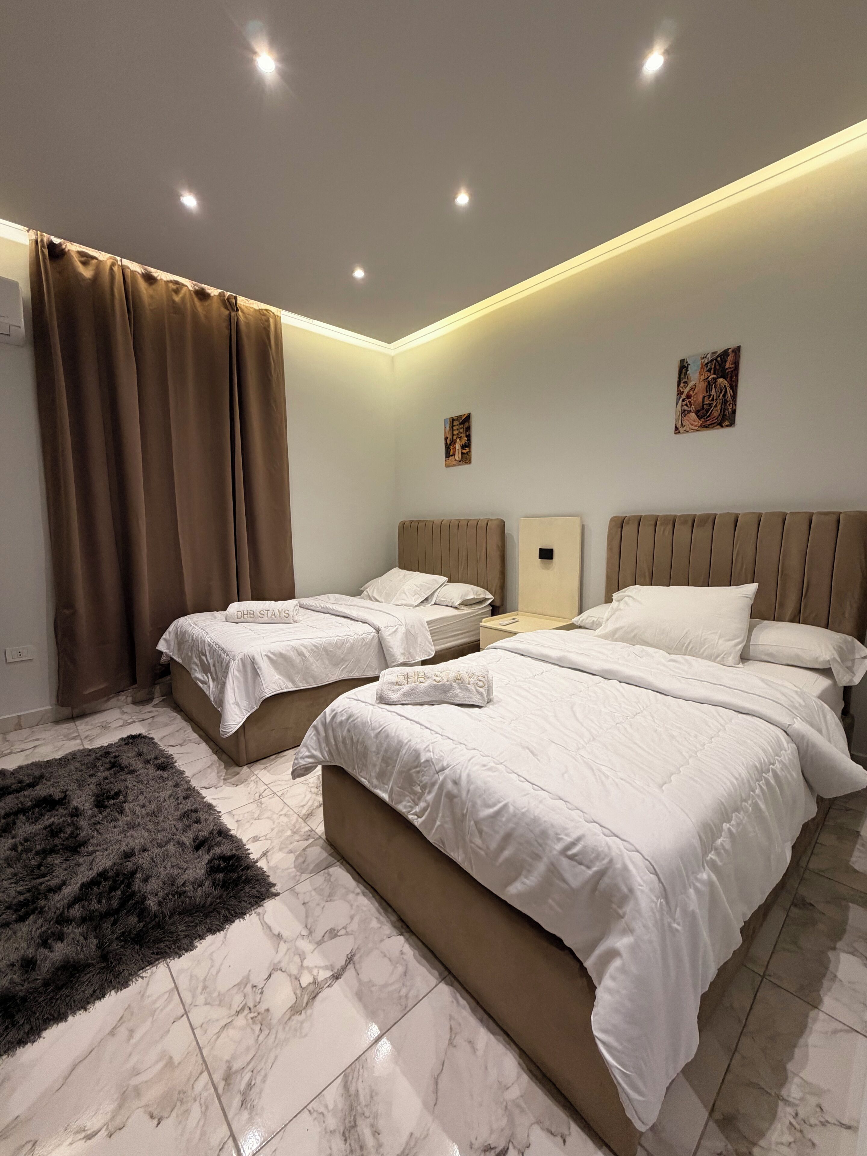 A hotel room with two beds, a large fluffy rug, and a marble floor.