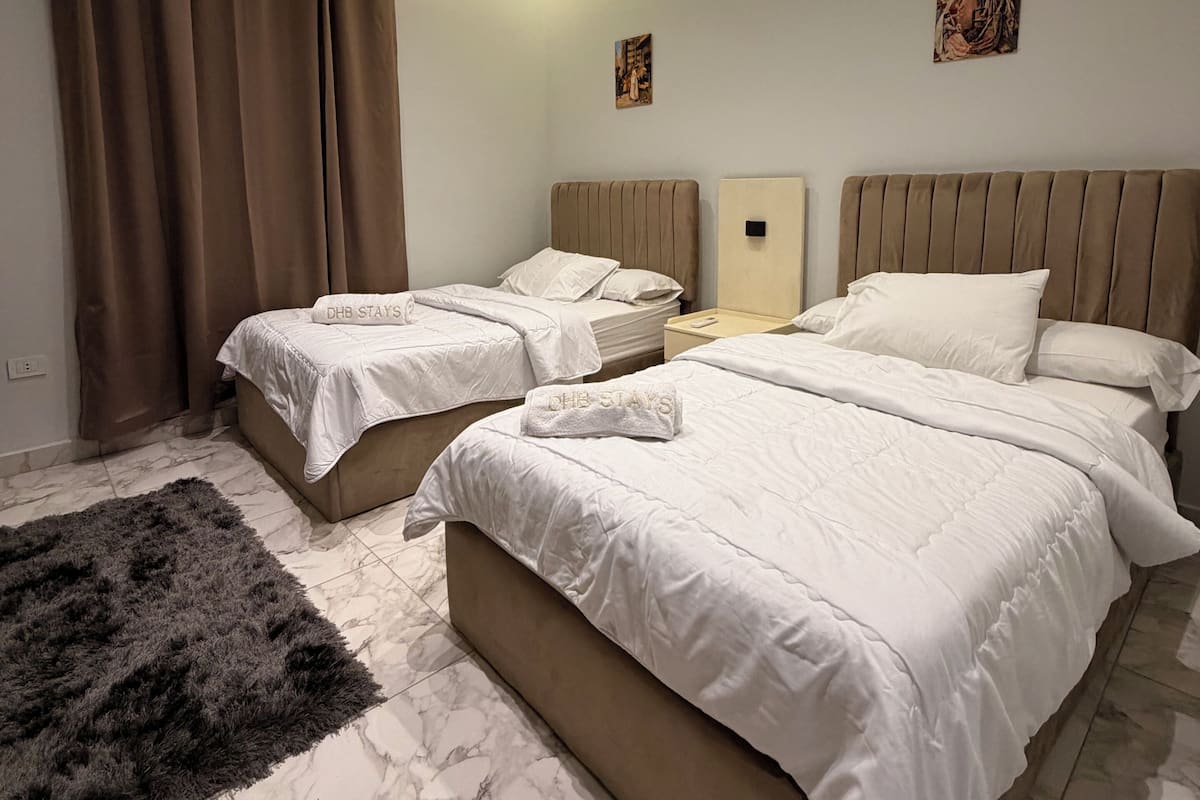 A hotel room with two beds, a large fluffy rug, and a marble floor.