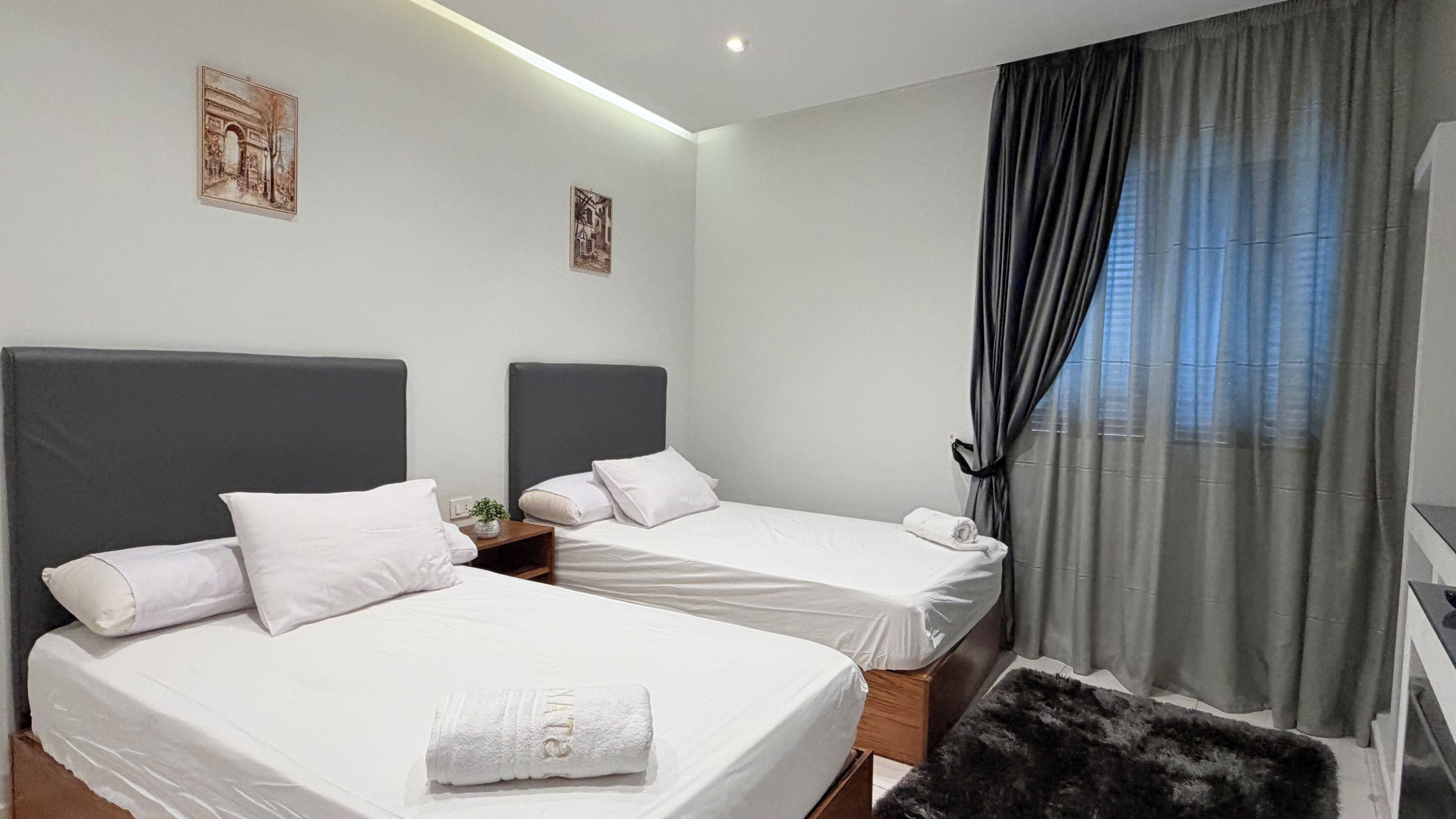 A hotel room with two beds, a small table, and a window with curtains.