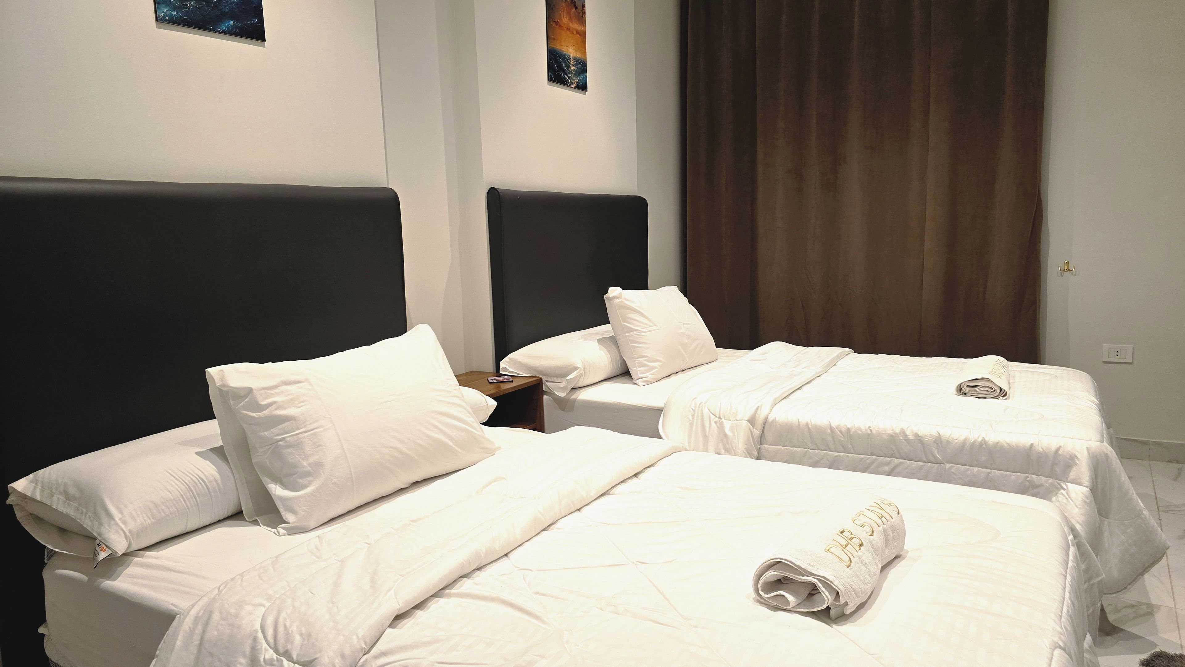 A hotel room with two beds, each with white bedding and pillows, and a dark headboard.