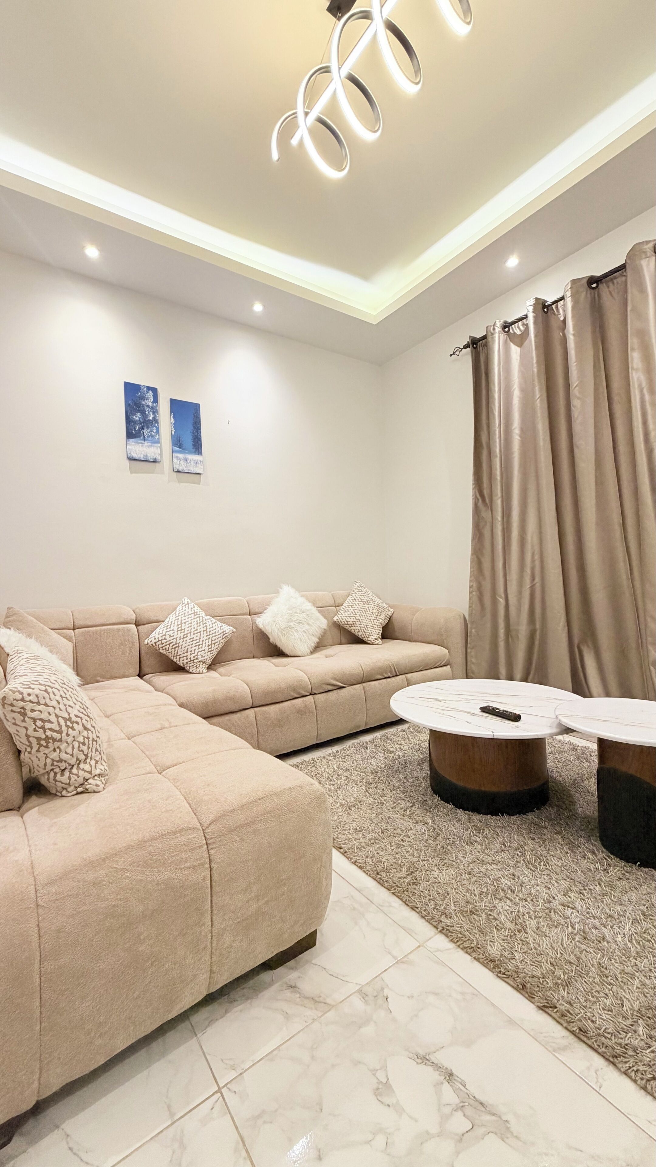 A modern living room with a sectional sofa, two side tables, and a chandelier.