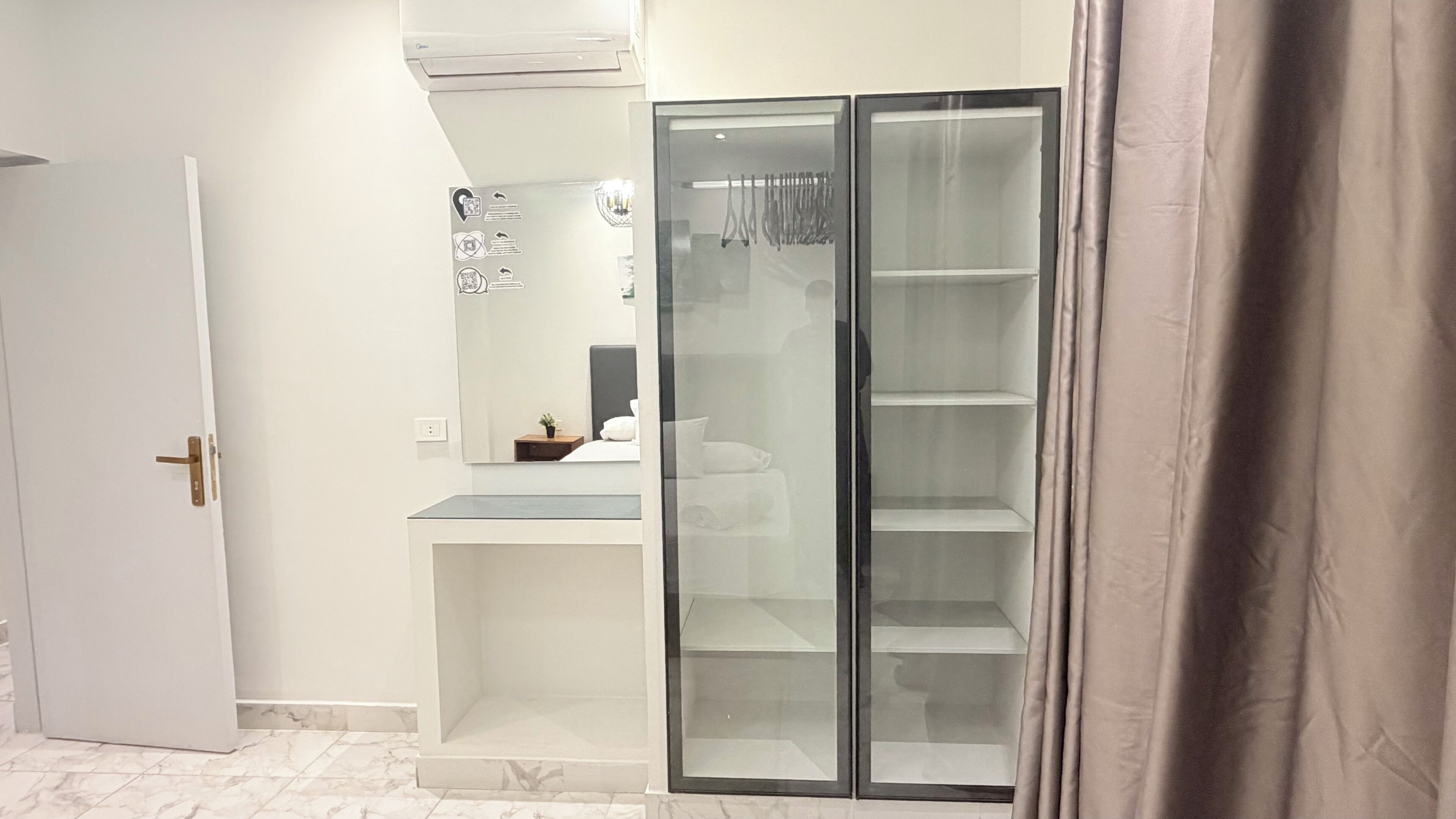 Une pièce avec une porte blanche, une armoire à façade en verre et un sol carrelé de marbre.