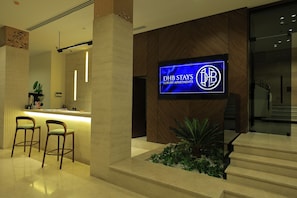 A reception area with a counter, two bar stools, a potted plant, and a sign for DHB Stays Luxury Apartments. - DHB STAYS DOWNTOWN (Cairo)