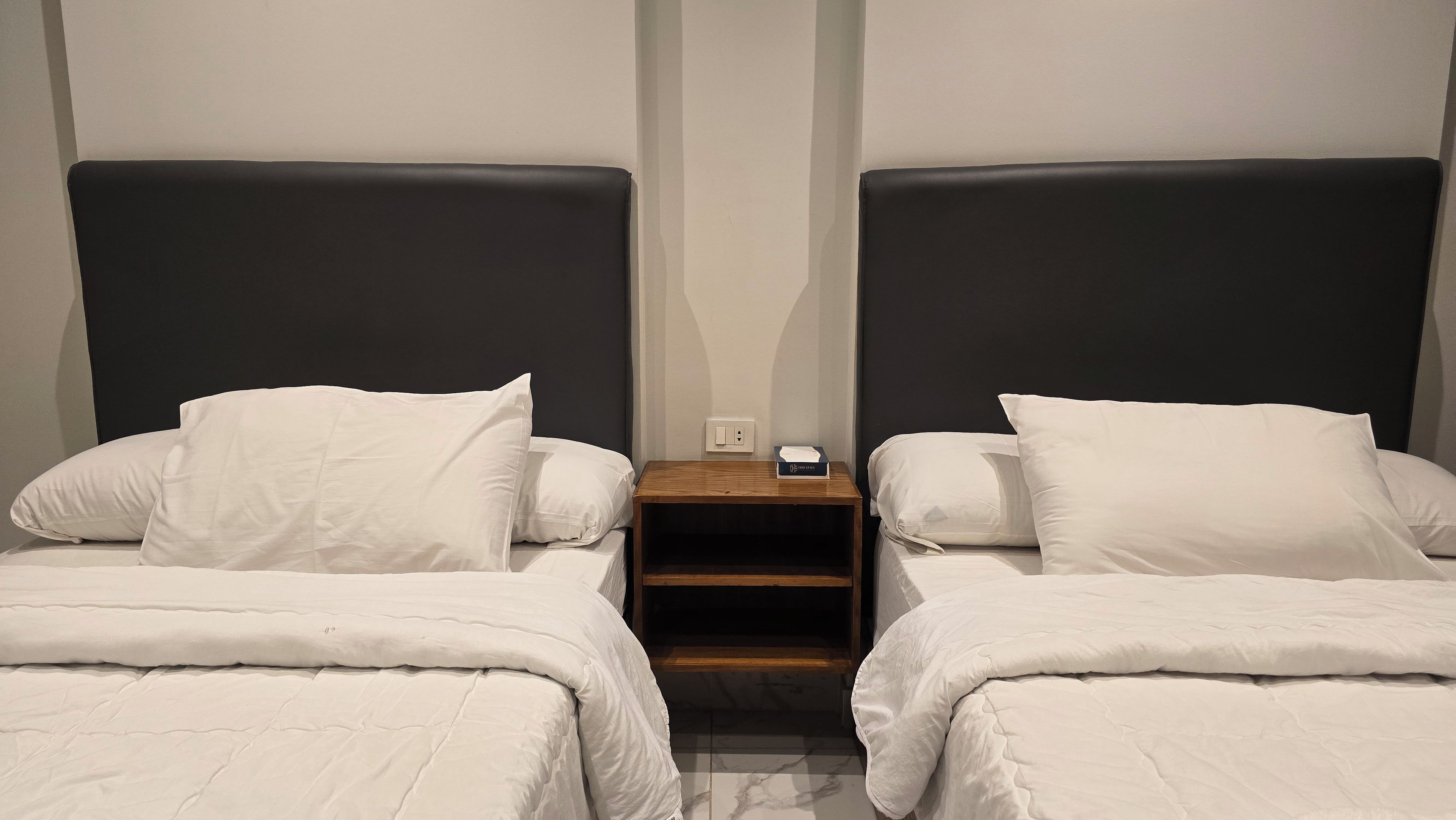 A hotel room with two single beds, each with white bedding and a dark headboard.