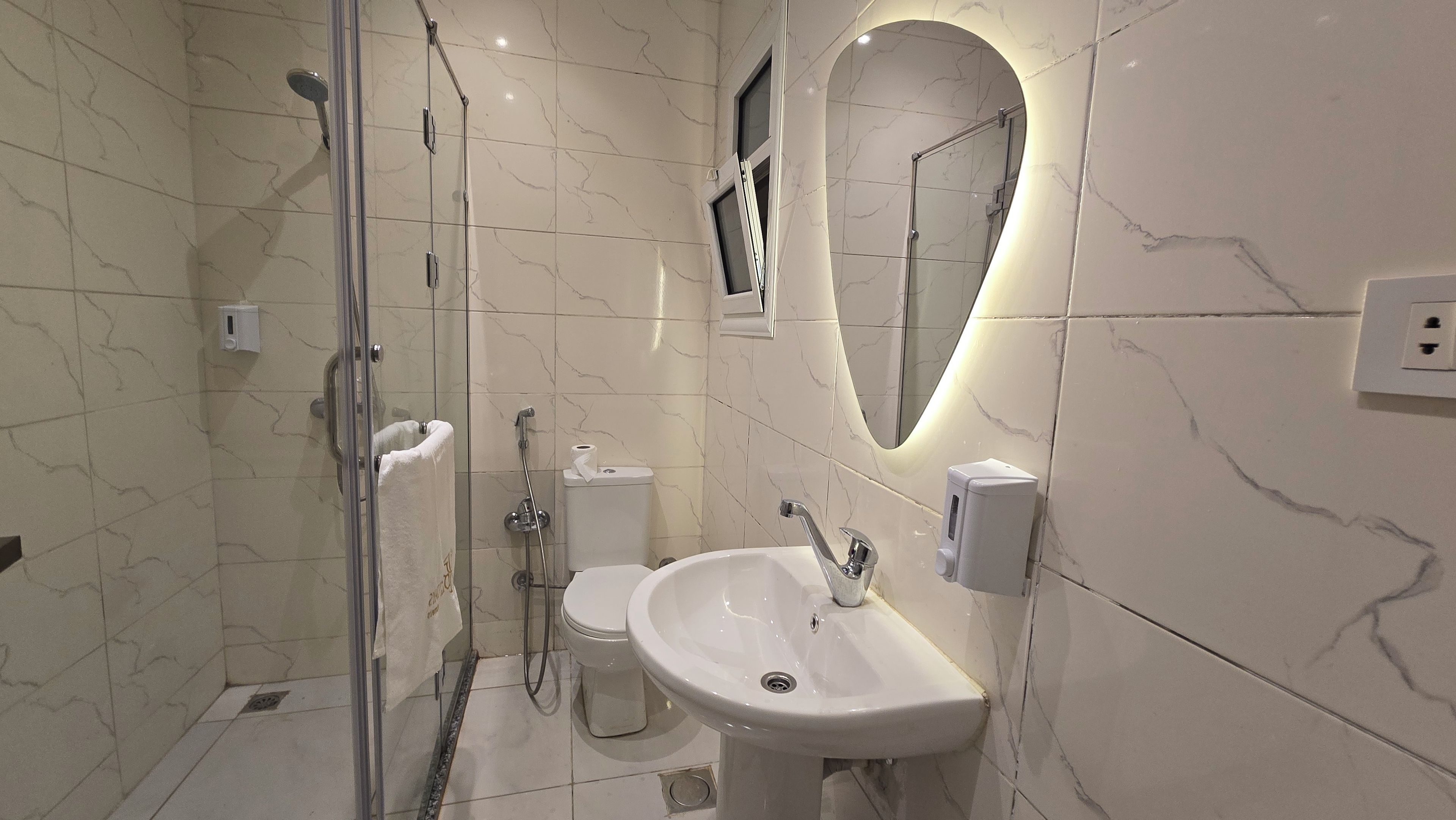 A modern bathroom with a glass-enclosed shower, a white sink, and a marble-tiled wall.