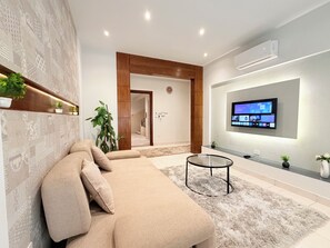 Una sala de estar moderna con un sofá seccional color beige, una mesa de centro de vidrio y un televisor de pantalla plana montado.