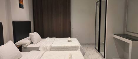 Habitación de hotel con dos camas, una cortina oscura, cabina de ducha de vidrio y un cuadro en la pared.