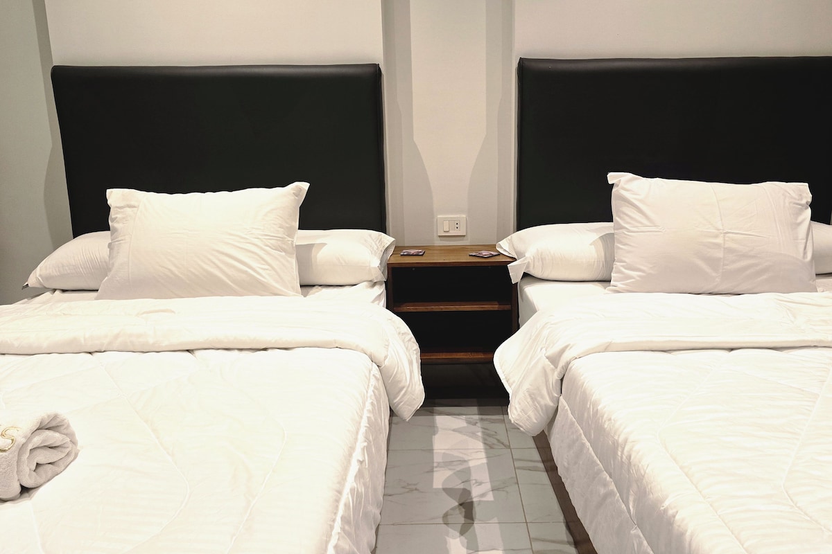 Een hotelkamer met twee éénpersoonsbedden, een nachtkastje en een stopcontact.