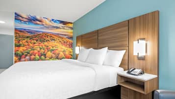 Une chambre d’hôtel avec un grand lit, une table de chevet avec un téléphone, une lampe fixée au mur et une fresque murale représentant un paysage automnal.