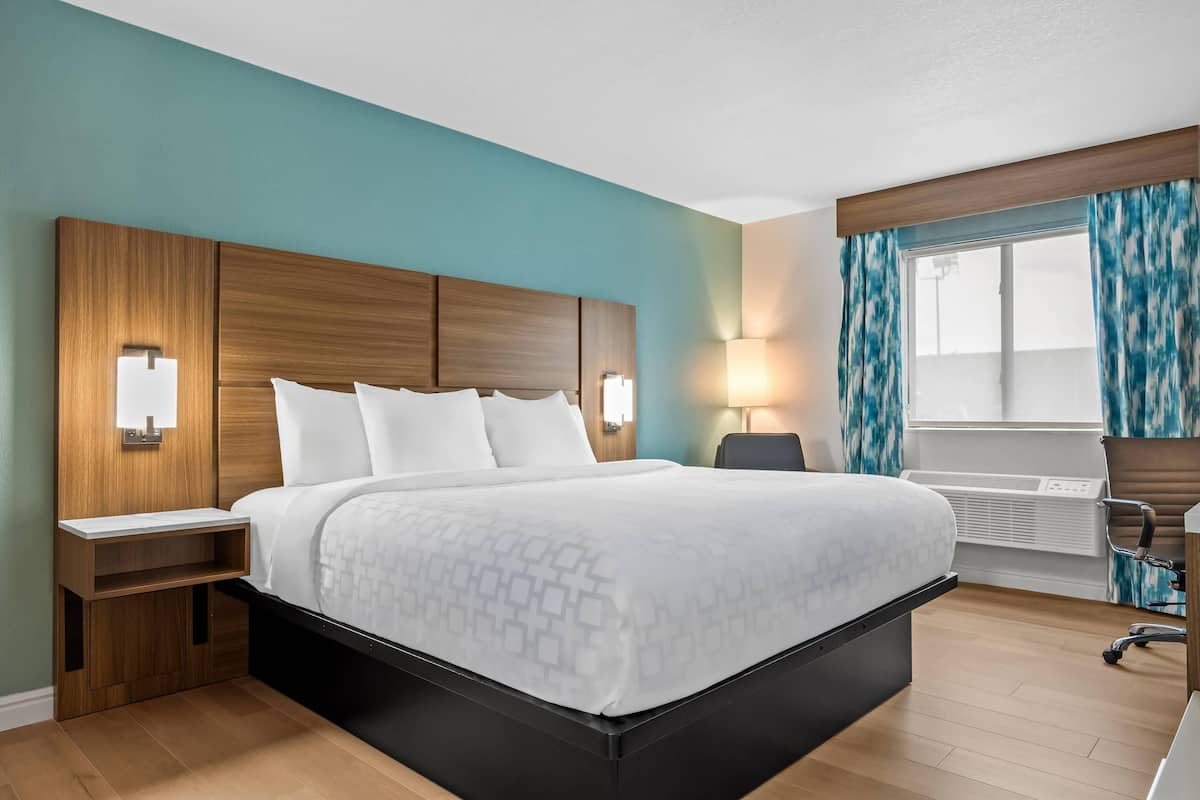A hotel room with a large bed, bedside tables, a desk, and a window with curtains.