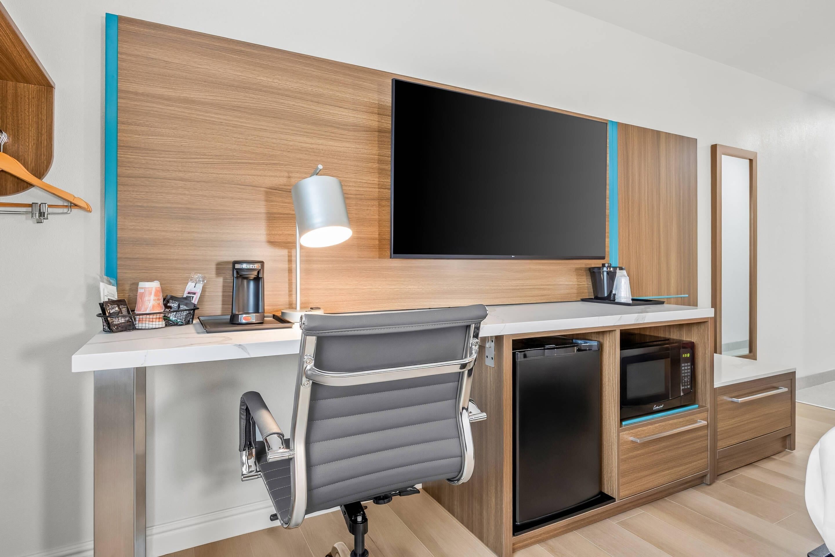 Una habitación de hotel moderna con escritorio, televisión montada, microondas y cafetera.