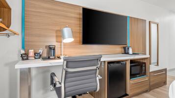 Una habitación de hotel moderna con escritorio, televisión montada, microondas y cafetera.