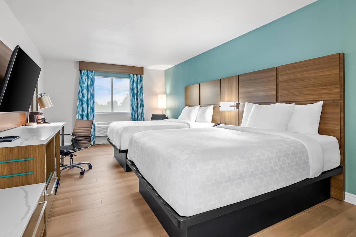 A hotel room with two beds, a desk with a TV, a chair, and a window with curtains.
