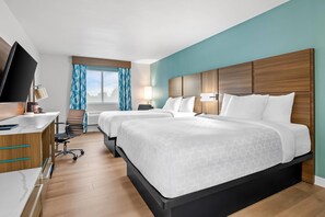 A hotel room with two beds, a desk with a TV, a chair, and a window with curtains. - Clarion Pointe Springfield Southeast (Springfield)