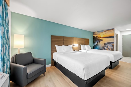 A hotel room with a bed, bedside table, lamp, and a painting of a sunset.