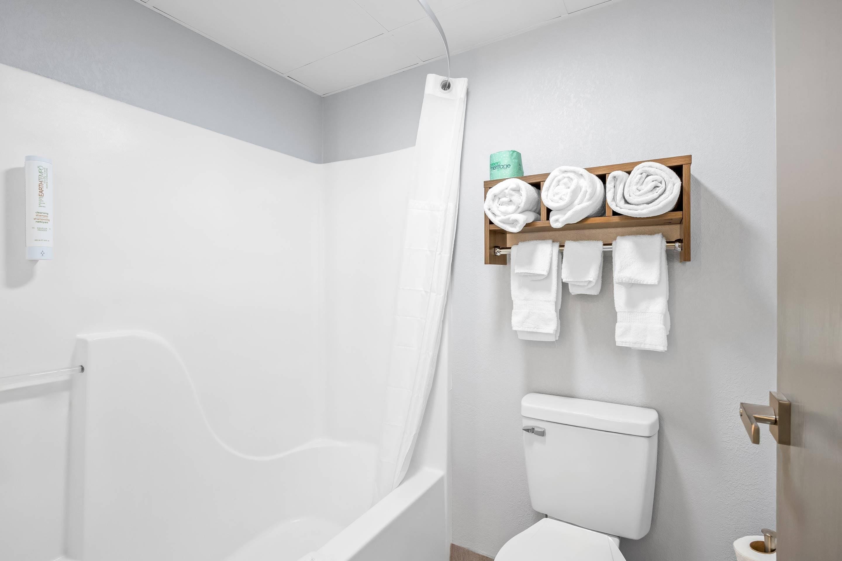 A bathroom with a shower, toilet, and a shelf with towels.