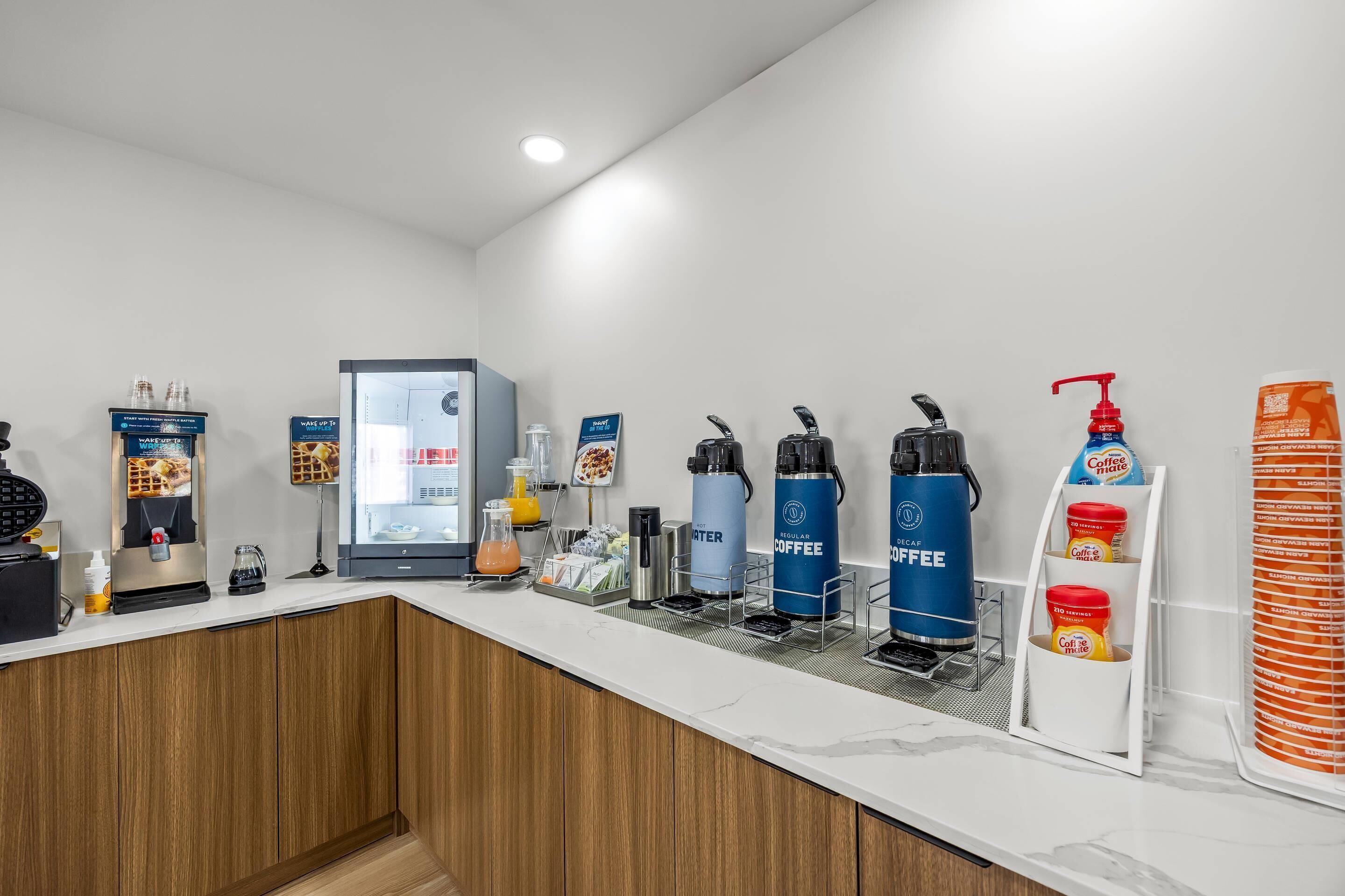 Eine Kaffeestation mit verschiedenen Kaffeeautomaten, einem Waffeleisen und einem Kühlschrank.