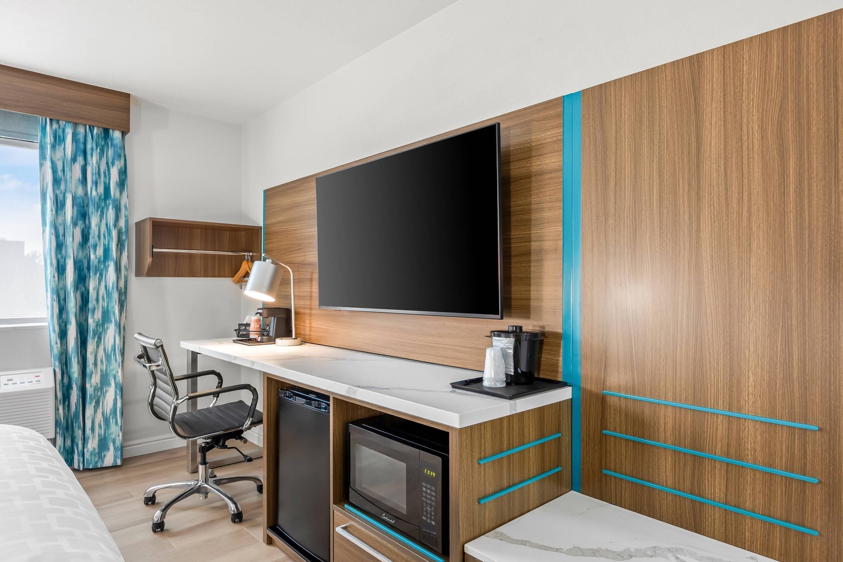 Una camera d'hotel moderna con TV a schermo piatto, una scrivania con lampada, un forno a microonde e un lavastoviglie integrato.